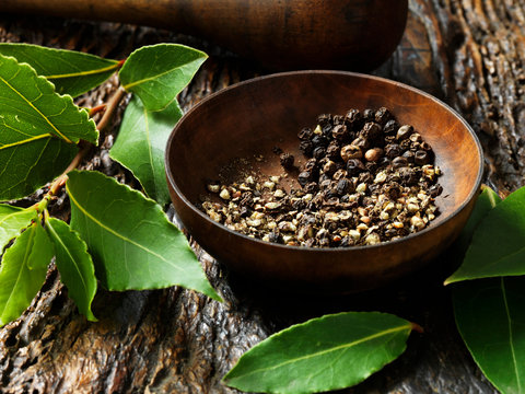 Crushed peppercorns in bowl, bay leaves on rustic wooden surface