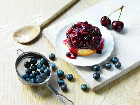 Morello cherry and blueberry sponge, fresh cherries and blueberries, wooden spoon with flour, white washed wooden board and wooden table