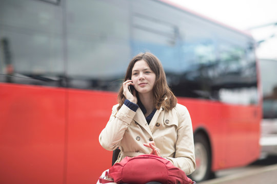 Young woman using wheelchair talking on smartphone at city bus station