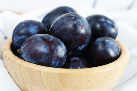 Fresh ripe plums in wooden bowl