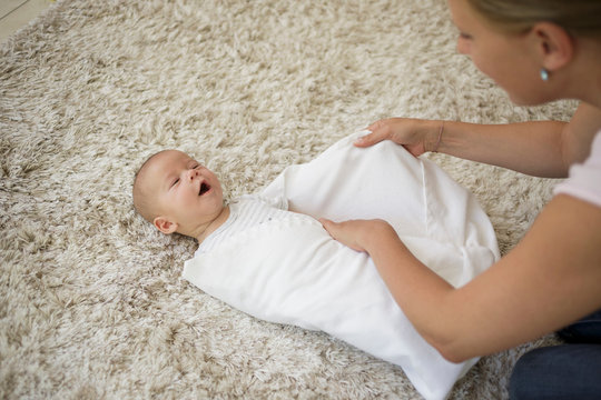 Swaddling Step 5. Mother wrapping and tucking in baby boy with blanket