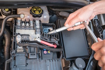 Hands checking the bolt of the battery with a wrench in a modern car engine