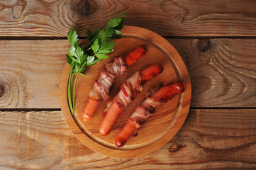 grilled sausages wrapped in bacon on wooden background
