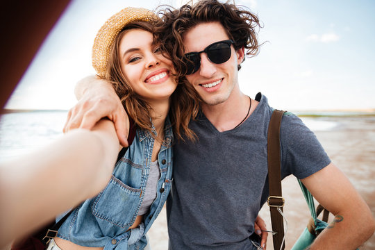 Smiling couple hugging and taking selfie on the beach