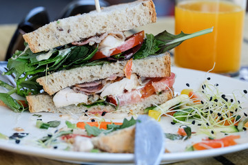 Club sandwich with vegetables, chicken and bacon on a white plate in focus