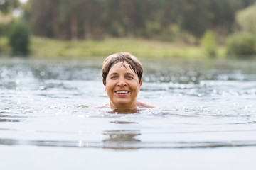 Healthy senior woman swimming in the lake or river. Happy elderly lady enjoying active summer vacation. Sportive lifestyle. Active retirement concept.

