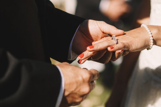 Groom puts a wedding ring over bride's finger holding it tender