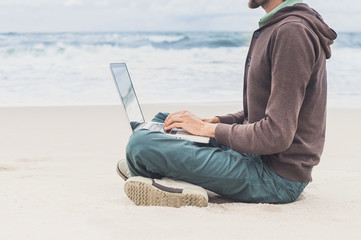 Young man working on laptop while sitting on the beach, freelance working, social networks concept
