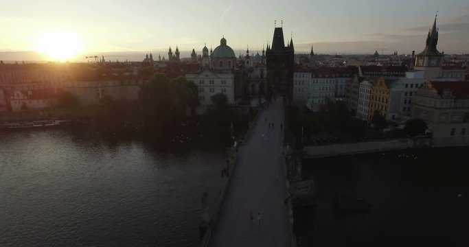 Aerial camera flies along the Charles Bridge towards the Old Town of Prague. Shot as the sun rises behind the city