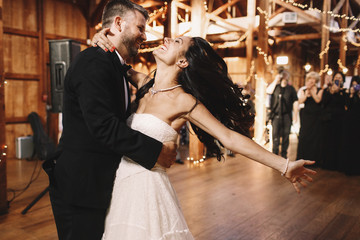 Bride shakes her dark hair while dancing with a groom in wooden