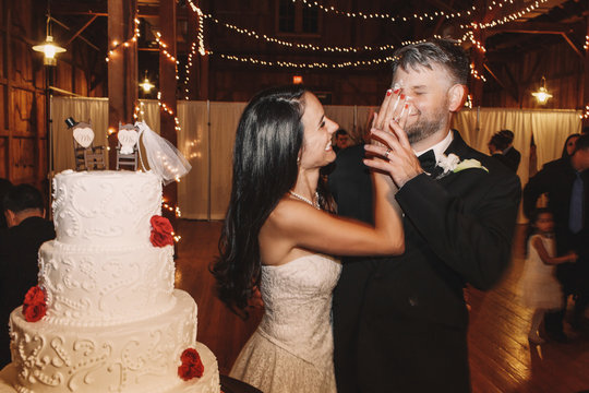 Smiling Brunette Bride Put A Wedding Cake Over Groom's Face