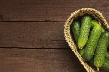 Cucumbers in a basket on wooden background. Free space for text . Top view
