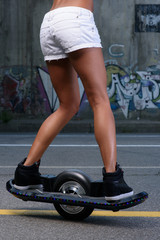 sporty athletic caucasian cute teen riding electric onewheel skateboard having fun in the street posing and hold in her hands