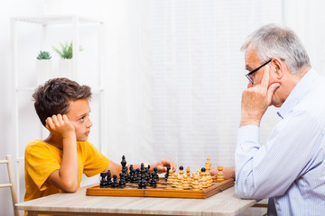 Grandfather and grandson are playing chess at home.