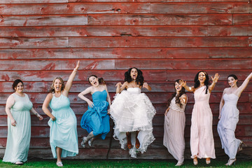 Bride in leather boots and bridesmaids in pastel dresses jump be - obrazy, fototapety, plakaty