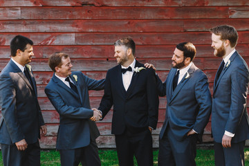 Groomsmen in blue suits greet groom while posing before a wooden