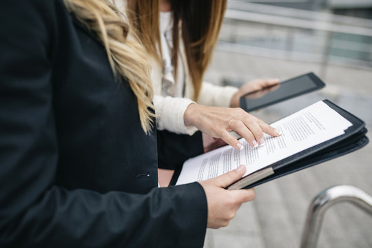Two businesswomen with digital tablet and documents outdoors