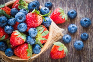 Blueberries and strawberry in wooden bowl on wooden table background