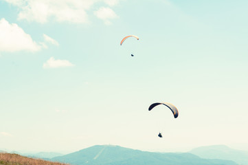 Two paragliders in sky with hills in background