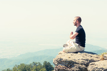 Young man meditating on top of the mountain
