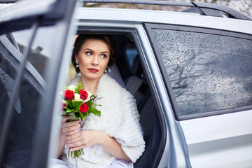 Beautiful bride sits in white car holding her bouquet of roses