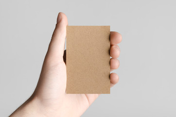 Kraft Business Card Mock-Up (85x55mm) - Male hands holding a kraft card on a gray background.