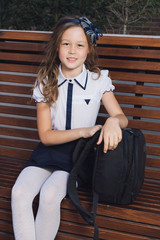 schoolgirl in uniform waiting for the bus to school. Schoolgirl in a darkly blue skirt, a white blouse and tights, in black shoes whith a black backpack