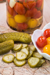 Pickles on a cutting board and bowl with cherry tomatoes pickles.
