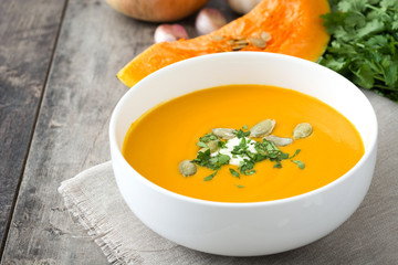 Pumpkin soup in bowl and ingredients on rustic wood
