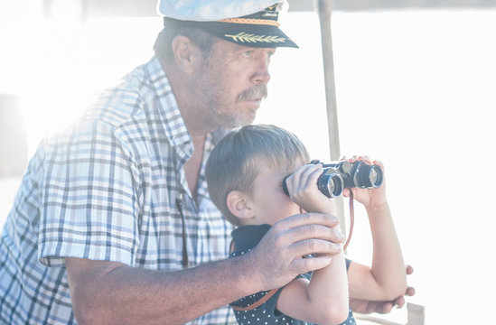 Boat captain with boy tourist looking through binoculars on boat trip, Cape Town, South Africa