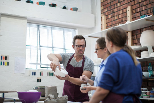 Male potter showing trainees bowl in workshop