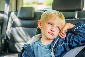 Young boy sitting in back of vehicle, bored expression