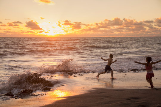 Girl and brother running on beach at sunrise, Blowing Rocks Preserve, Jupiter Island, Florida, USA