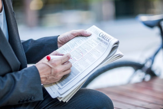 Neck down view of businessman circling job vacancies in newspaper