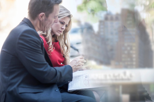 Businessman and woman reading newspaper and chatting in city park