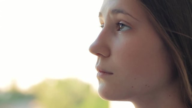 sad alone hope - Closeup side profile portrait of young woman outdoors serious pensive. Unhappy teen girl face thinking and looking ahead