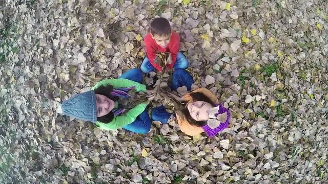 Top view of three happy children throwing autumn leaves high. 