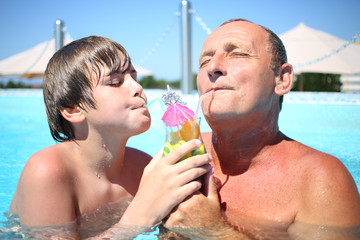 Portrait of a happy senior and young boy drinking a tropical cocktail at the swimming pool