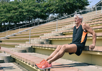 Muscular senior athlete doing triceps exercise on stadium