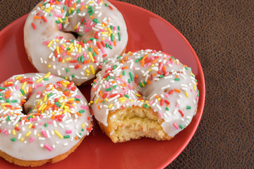 Three white frosted cake donuts with colorful sprinkles, bite taken out of one
