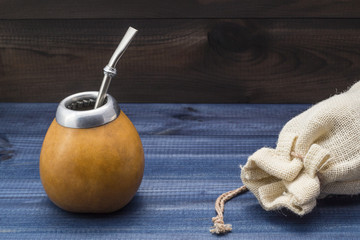 yerba mate with gourd matero, bombila, wooden spoon and linen bag on wooden background.
