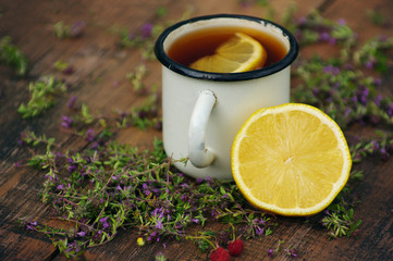 Tea in an iron mug, lemon, medicinal herbs on a wooden surface.