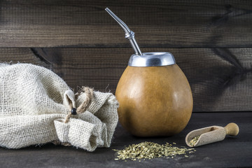 yerba mate with gourd matero, bombila, wooden spoon and linen bag on wooden background.