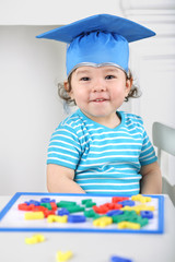 Portrait of laughing child in blue graduation hat sitting at table with children magnetic board with colored letters