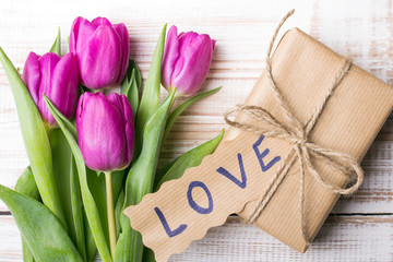 word LOVE and bouquet of tulips on wooden background
