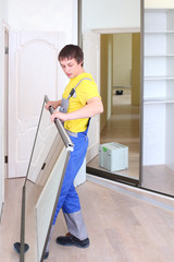 Young worker holding mirrored door on sliding wardrobe in room