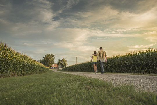 Caucasian father and daughter walking on dirt path by corn field - Powered by Adobe