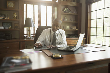 Black doctor using digital tablet in office
