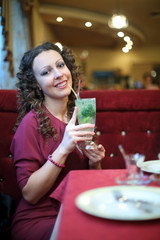 Beautiful girl with curly hair holding cocktail while sitting at table in restaurant
