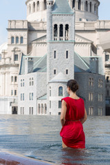 Young woman is standing into the fountain near the church at autumn day.